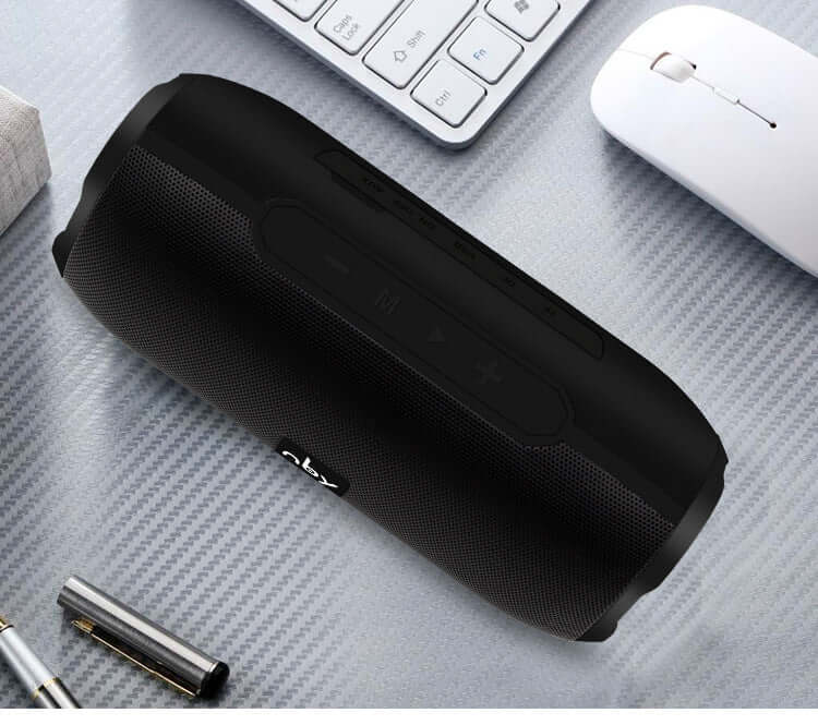 Bluetooth wireless speaker in black with control buttons on top, placed on a textured surface.