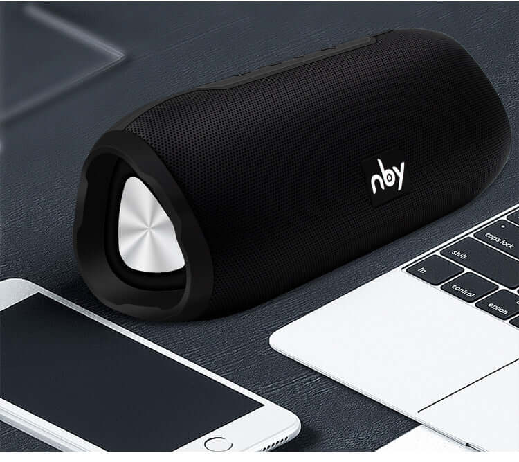 Bluetooth wireless speaker on a desk next to a smartphone and laptop, showcasing its sleek design and portable features.
