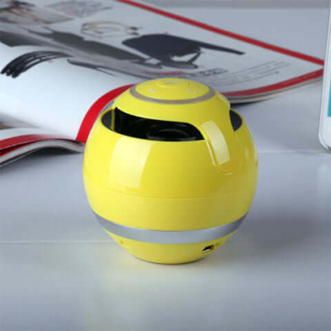 Wireless bluetooth speaker in vibrant yellow color on a table beside a magazine.
