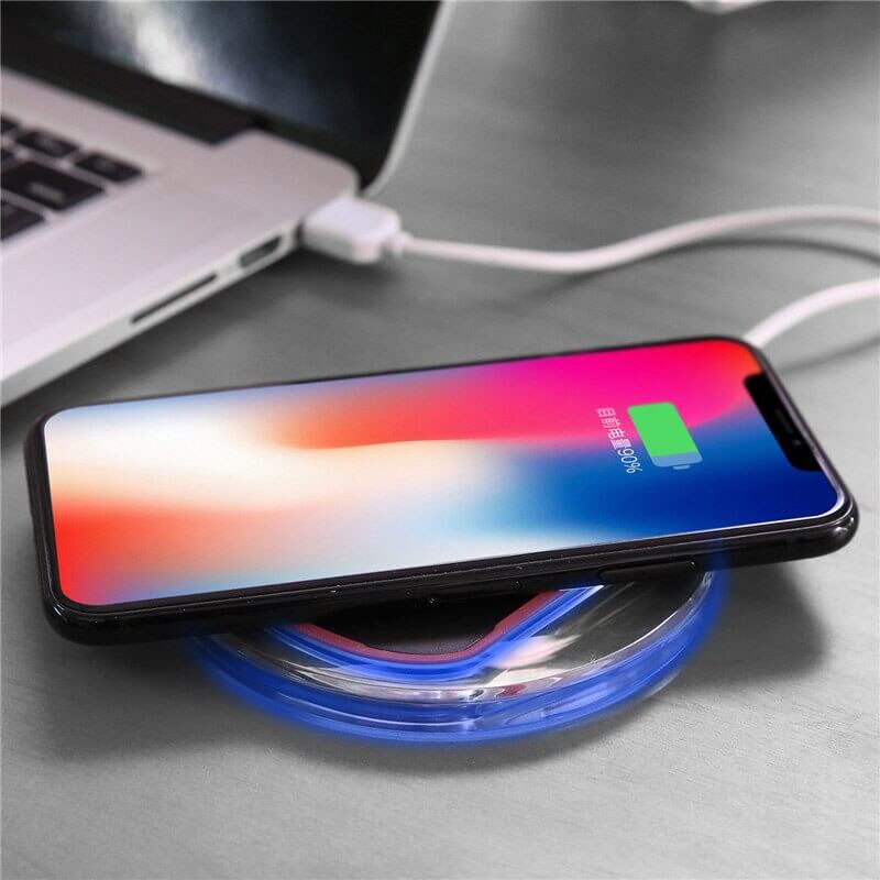 Wireless charger wireless receiver charging smartphone on a sleek charging pad with laptop in background.