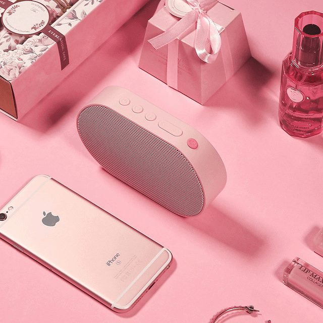 Pink Bluetooth stereo smart speaker on a pink surface with a smartphone and beauty products.