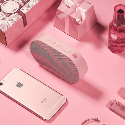 Pink Bluetooth stereo smart speaker on a pink surface with a smartphone and beauty products.