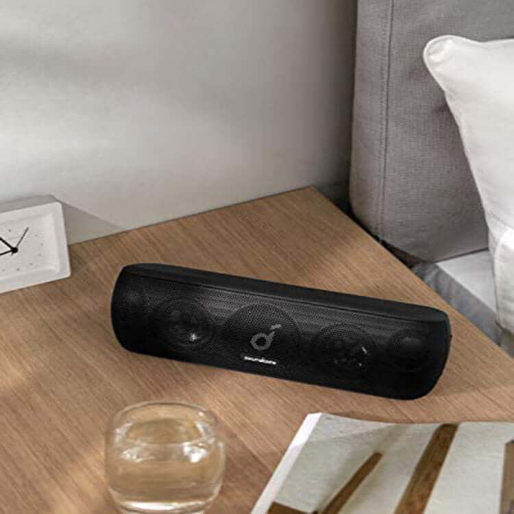 Subwoofer Bluetooth Speaker on a wooden table next to a glass and clock, showcasing its sleek design.